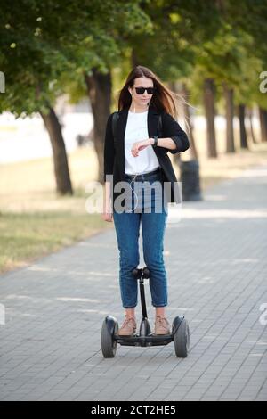 Jeune femme d'affaires élégante regardant la montre-bracelet tout en montant sur le gyroscope Banque D'Images