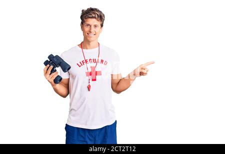 Jeune homme beau portant un t-shirt de maître-nageur à l'aide de jumelles souriant heureux en pointant avec la main et le doigt sur le côté Banque D'Images