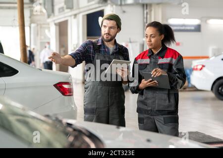 Jeune réparateur en uniforme décrivant le problème de sa collègue féminine voiture Banque D'Images