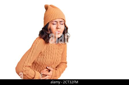 Jeune belle femme de race mixte portant un chandail en laine et un chapeau d'hiver avec main sur l'estomac parce que l'indigestion, la maladie douloureuse sentiment malaise. Ache co Banque D'Images