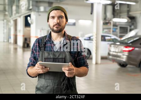 Jeune employé barbu d'un service de voiture contemporain utilisant une tablette dans atelier Banque D'Images