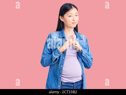 Jeune belle chinoise femme enceinte s'attendant à bébé mains ensemble et les doigts croisés souriant détendu et gai. Succès et optimiste Banque D'Images