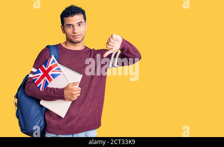 Hispaniques beau jeune homme échange étudiant tenant le drapeau du royaume-uni avec le visage en colère, signe négatif montrant l'aversion avec le pouce vers le bas, concept de rejet Banque D'Images