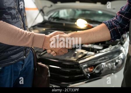 Jeune technicien contemporain de service de voiture secouant la main de l'homme client Banque D'Images