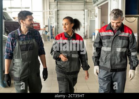 Trois travailleurs interculturels du centre de maintenance automobile se déplacent le long de l'atelier Banque D'Images