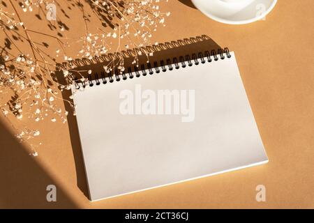 Maquette de bloc-notes vierge sur fond orange avec fleurs de gitsophila. Vue de dessus, plat, espace de copie Banque D'Images