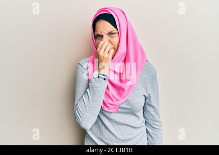 Jeune femme caucasienne portant un foulard islamique traditionnel hijab qui sent quelque chose de stini et de dégoûtant, une odeur intolérable, qui retient l'haleine avec les doigts Banque D'Images