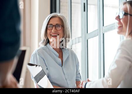 Bonne vieille femme mentor en train de parler à de jeunes stagiaires lors d'une réunion de groupe au bureau. Banque D'Images