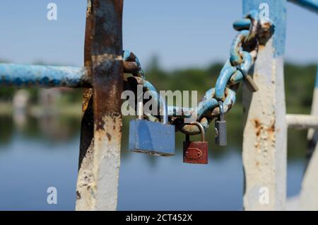 Plusieurs cadenas pendent d'une ancienne chaîne. Cadenas de mariage enchaînés au pont de la ville. Symbole de l'amour et de la tradition de mariage ancienne. Vieux rouillé chéri l Banque D'Images