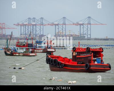Des bateaux de pêche en bois et un petit cargo amarrés à Siracha, en Thaïlande, avec le port commercial en arrière-plan, partiellement obscurci par le brouillard. Banque D'Images