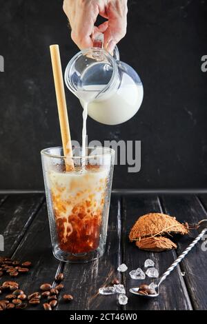 Café glacé de style thaï avec lait de coco et grains de café sur fond noir en bois. Banque D'Images