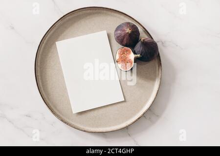 L'automne encore la vie. Maquette de carte de vœux vierge, figues coupées fruit et plaque en céramique sur fond de table en marbre blanc. Concept d'automne et de Thanksgiving, style Banque D'Images