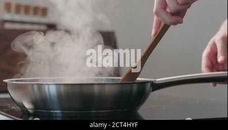 homme main en mouvement quelque chose avec une spatule en bois dans un poêle à frire, photo large Banque D'Images