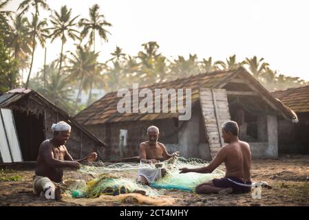 Pêcheurs faisant des filets de pêche sous des palmiers tropicaux au lever du soleil à Kappil Beach, Varkala, Kerala, Inde Banque D'Images