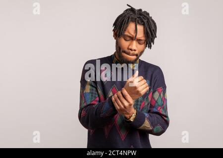 Frustré triste homme africain avec des dreadlocks grimaquant touchant son poignet, sensation soudaine de douleur aiguë, syndrome de tunnel, blessure professionnelle. Salle de studi Banque D'Images