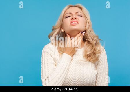 Gros plan déçu femme avec des cheveux blonds touchant le cou, sensation de douleur dans les glandes, amygdalite, douleur à avaler. Prise de vue en studio isolée sur bleu Banque D'Images