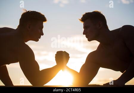 Rivalité, vs, défi, lutte de main. Coucher de soleil, lever du soleil. Hommes mesurant les forces, les bras. Deux hommes luttant. Silhouette de mains qui rivalisent Banque D'Images