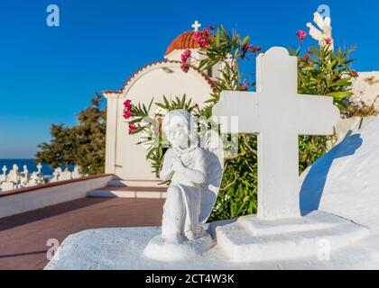 Statue d'ange et de Croix de prière avec église traditionnelle avec dôme rouge en arrière-plan, île de Karpathos, Grèce Banque D'Images