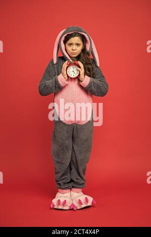 Alarme du matin. Jour normal de début. Adorable réveil à motif lapin. Petite fille en costume de lapin. Enfant lapin kigurumi. Pyjama fille à motif lapin. Bunny rouge enfant fond. Bébé animal. Temps de comptage. Banque D'Images