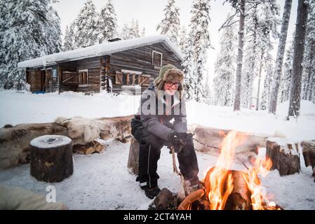 Personne assise à un feu de camp se réchauffant lui-même par un froid glacial en hiver dans le cercle arctique de Laponie, en Finlande Banque D'Images