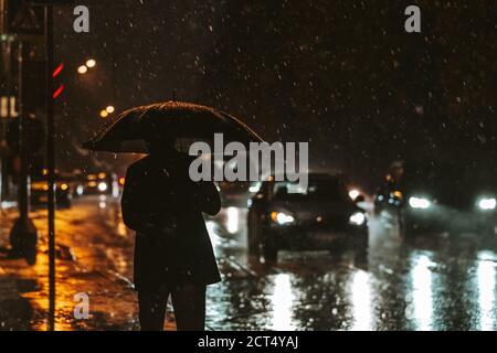 Silhouette d'un homme avec un parapluie dans le contre-jour des phares la nuit pendant une descente. Forte pluie dans la ville. Un piéton avec un parapluie Banque D'Images