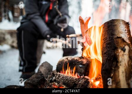 Personne assise à un feu de camp se réchauffant lui-même par un froid glacial en hiver dans le cercle arctique de Laponie, en Finlande Banque D'Images