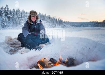 Personne assise à un feu de camp se réchauffant lui-même par un froid glacial en hiver dans le cercle arctique de Laponie, en Finlande Banque D'Images