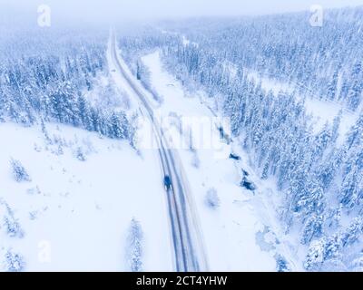 Antenne de voiture roulant sur une route dangereuse d'hiver à mauvaises conditions de glace à côté de la rivière gelée et de la neige couverte forêt Banque D'Images
