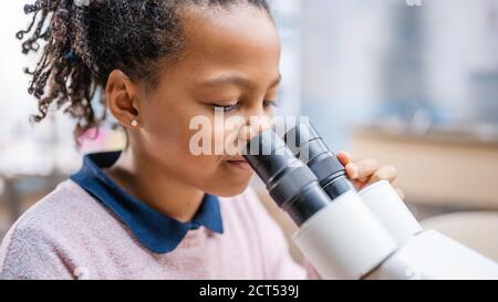 Portrait de Smart petite écolière regardant sous le microscope. Dans la salle de classe élémentaire Cute Girl utilise le microscope. Science DE LA TIGE, technologie Banque D'Images