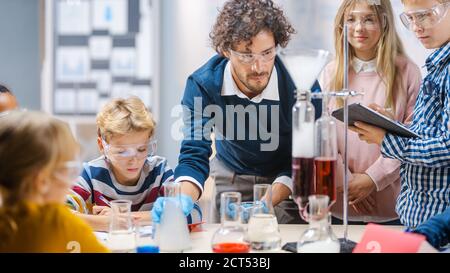 École élémentaire de sciences en classe: Un professeur enthousiaste explique la chimie à divers groupes d'enfants, leur montre comment mélanger les produits chimiques dans les béchers Banque D'Images