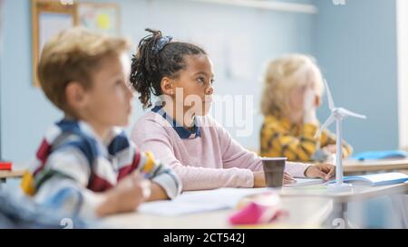 Dans la salle de classe de l'école primaire Brilliant Black Girl écoute attentivement un enseignant. Salle de classe junior avec groupe d'enfants lumineux travaillant Banque D'Images