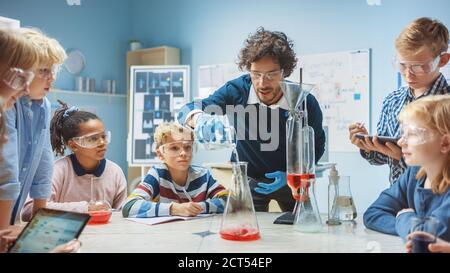 École primaire de chimie classe: Un professeur enthousiaste enseigne divers Groupe d'enfants montre Science réaction expérience en mélangeant des produits chimiques dans Banque D'Images