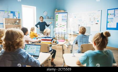 L'enseignant en informatique de l'école élémentaire utilise le tableau blanc numérique interactif pour Afficher les logiques de programmation dans une salle de classe pleine de Smart diverse Banque D'Images