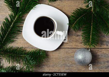 Branches de sapin avec aiguilles vertes, boules de Noël et une tasse de café sur une soucoupe sur fond de bois. Mise au point sélective. Banque D'Images