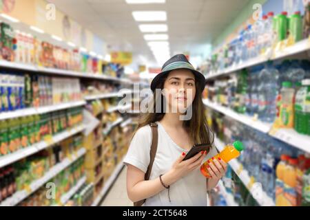 Jeune belle femme choisit une bouteille de jus dans le supermarché et vérifie le code QR sur l'étiquette. Le concept de technologie moderne et de shopping Banque D'Images