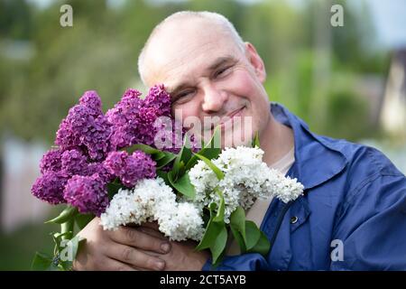 Homme âgé avec un bouquet de fleurs. Homme aux cheveux gris brutaux avec un beau lilas. Banque D'Images