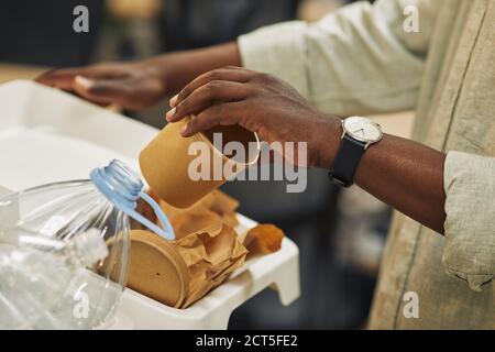 Gros plan d'un homme afro-américain méconnu qui met une tasse de papier dans le bac de tri des déchets dans le bureau, l'espace de copie Banque D'Images