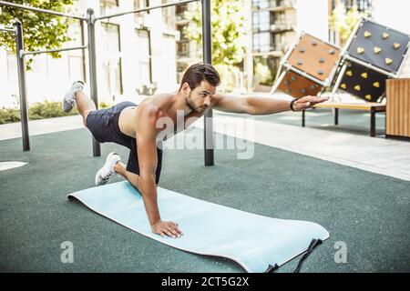 Jeune homme s'exerçant à l'extérieur. Le sportif se tient sur une jambe et la main est en position de planche. Corps d'entraînement. Exercice et entraînement. Faire de l'exercice seul Banque D'Images