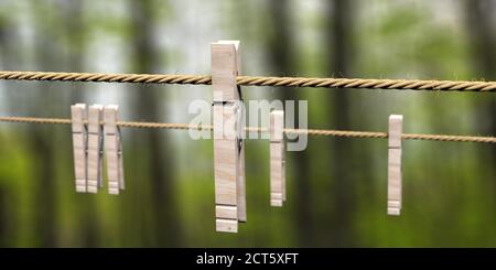 Épingles à linge sur corde de vêtements contre fond vert flou nature. Outils rétro de séchage Lauddy, crochets pour pendre des vêtements. illustration 3d Banque D'Images