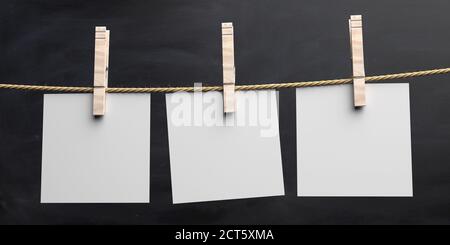 Des notes de papier vides tenant sur une corde à linge avec des épingles à linge en bois isolées sur fond noir. Balises vierges, modèle d'étiquette. illustration 3d Banque D'Images