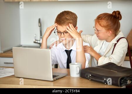 adorable redhead enfant fille soutient petit ami garçon travaillant sur ordinateur portable, elle est à l'écoute de ses problèmes au travail, les délais. à la maison Banque D'Images