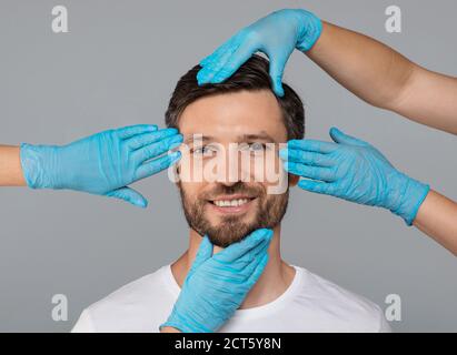 Mains dans des gants de protection touchant le visage d'homme souriant Banque D'Images