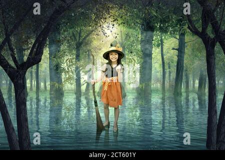 Petite fille asiatique sorcière avec un bâton magique debout au-dessus l'eau sur la forêt Banque D'Images