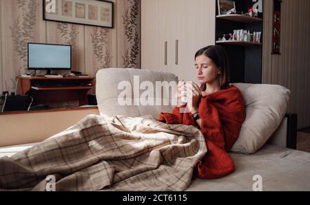 Femme malade et grippe. Pris au froid. Femme se sentant froide avec une couverture reposant sur le canapé à la maison Banque D'Images