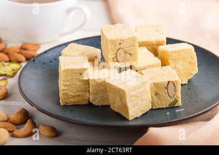 papildi de soan traditionnel indien dans une assiette en céramique bleue avec amande, pistache, noix de cajou et une tasse de café sur fond blanc en bois avec orange Banque D'Images