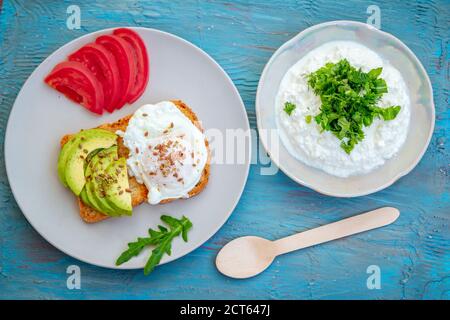 Griller avec des œufs pochés, des graines de lin, des tranches d'avocat et de tomate et du fromage cottage avec des feuilles d'arugula coupées sur une assiette. Repas sain pour le petit déjeuner. Banque D'Images