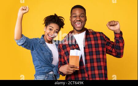 Joyeux couple afro-américain tenant des billets d'avion sur fond jaune Banque D'Images