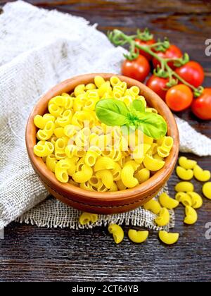 Pâtes Elbow avec basilic dans un bol en argile sur toile de raclage, tomates sur fond de bois Banque D'Images