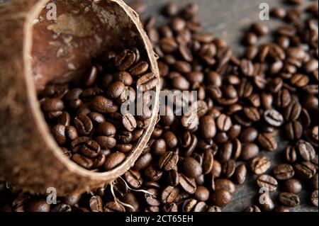 Grains de café arabica rôtis éparpillés sur une table en bois à partir d'une noix de coco. Grains de café frais. Banque D'Images