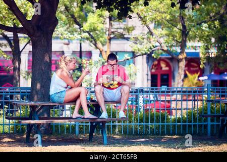 Montréal, Canada - juin 2018 : jeune couple assis dans le parc avec un smartphone et lisant un livre à Montréal, Québec, Canada. Relations, loisirs, Banque D'Images